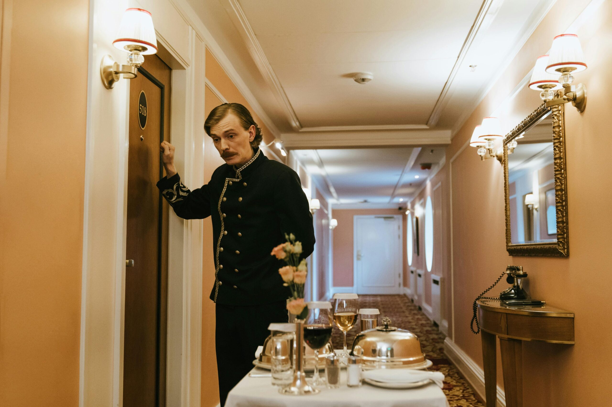 A hotel staff member in uniform serves room service with a trolley in a luxurious hallway.